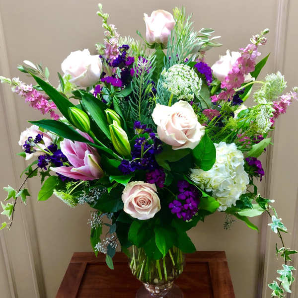 Mixed bouquet of pale pink roses, lilies, and purple flowers in a glass vase