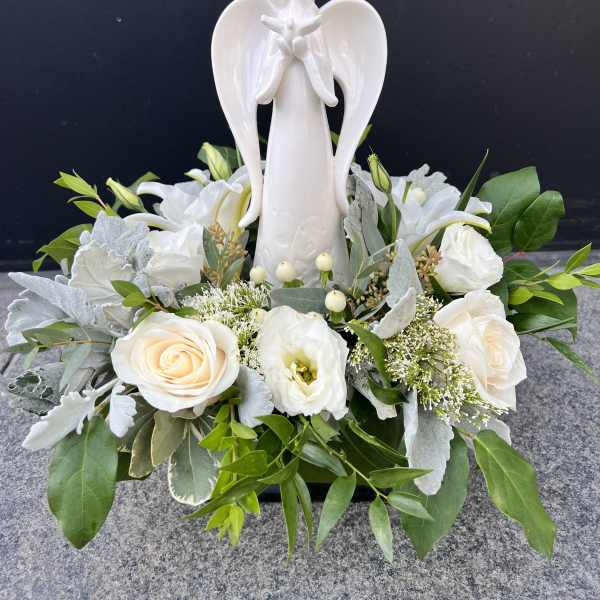 White angel figurine surrounded by white roses and greenery