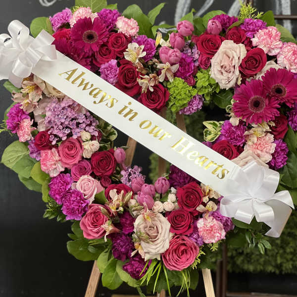 Heart-shaped floral wreath with pink and red roses and a white ribbon