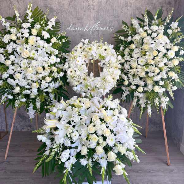 White floral funeral wreaths and sprays on stands with a large floor arrangement