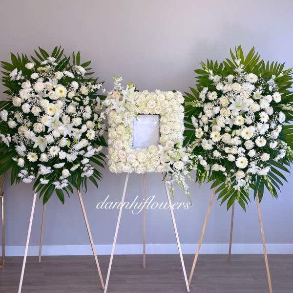 Three white floral funeral sprays on easels, with a rose frame in the center