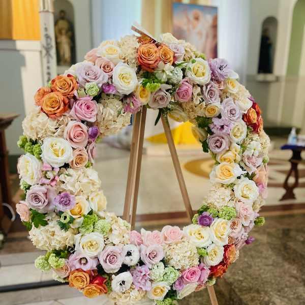 Large circular floral wreath on a wooden stand with pastel roses and hydrangeas