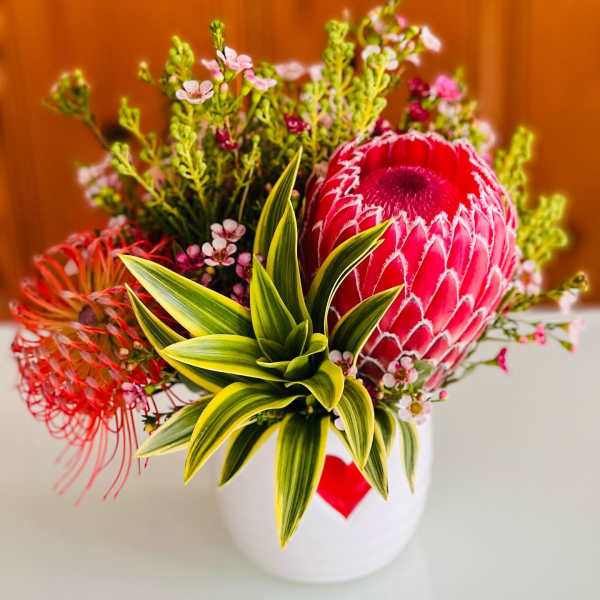 Bright tropical bouquet with a large pink protea in a white vase