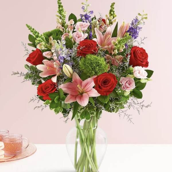 Bouquet of red roses, pink lilies, and purple flowers in a clear glass vase