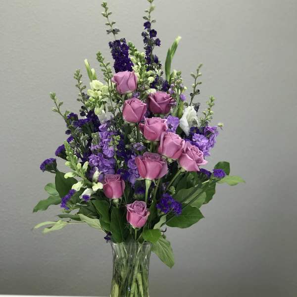 Pink roses and purple flowers arranged in a clear glass vase