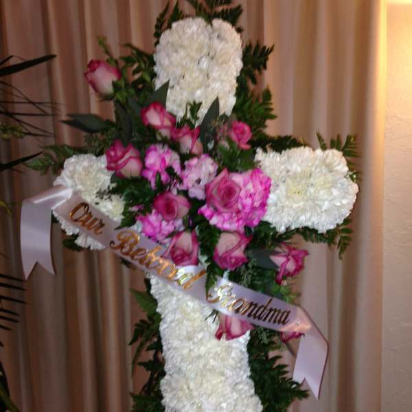 White floral cross with pink roses and ribbon on an easel