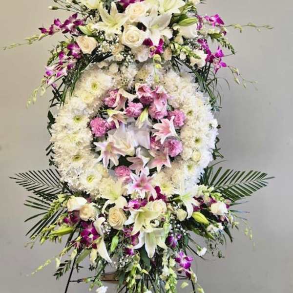 Large standing floral wreath with white lilies, roses, and pink orchids