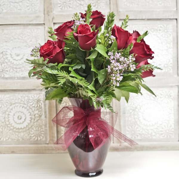 Red roses arranged in a glass vase with a burgundy ribbon