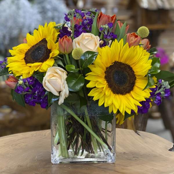 Sunflowers, peach roses, and purple flowers in a clear glass vase