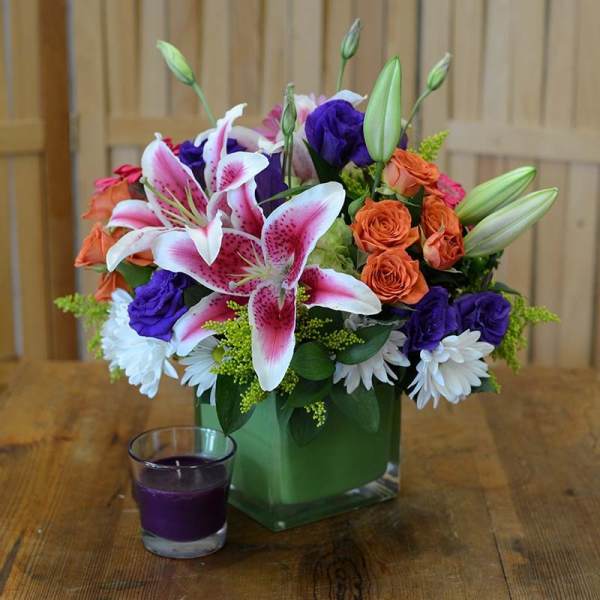 Mixed bouquet in a green glass vase with lilies, roses, and daisies