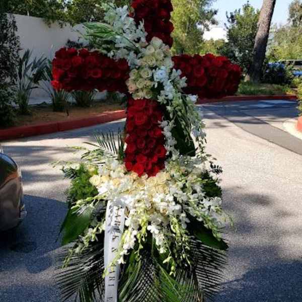 Tall standing cross of red and white flowers on an easel with cascading white blooms