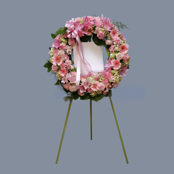 Pink floral funeral wreath on a standing easel with ribbon