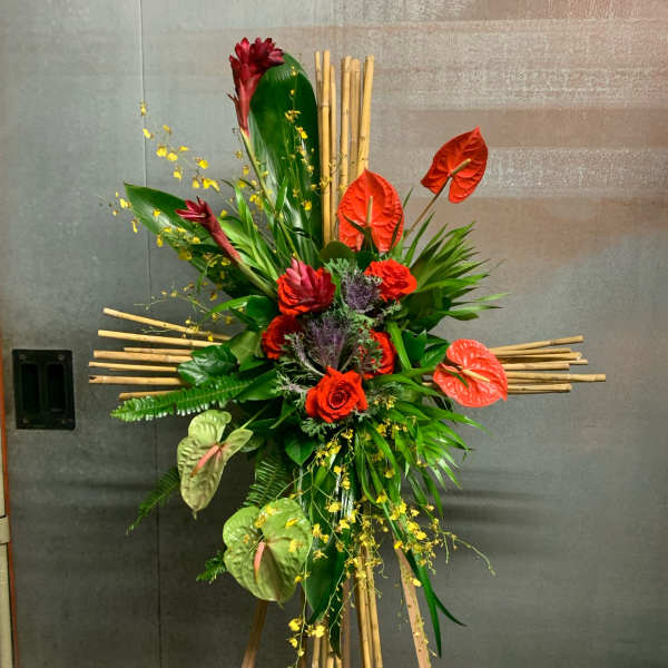 Tall tropical floral arrangement with red anthuriums and roses on a bamboo stand