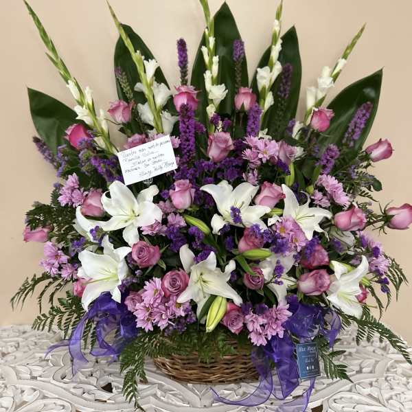 Basket arrangement of white lilies, pink roses, and purple flowers