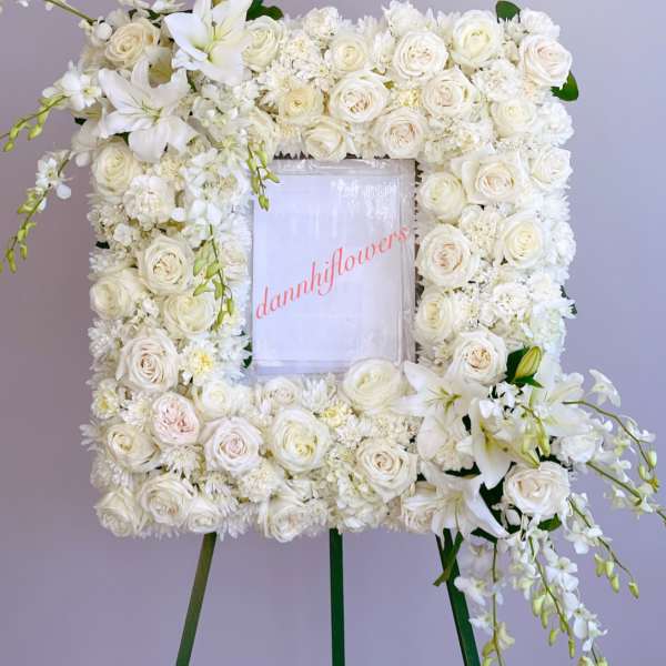 White floral wreath on an easel with roses and lilies