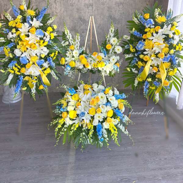 Three yellow, white, and blue floral funeral sprays with ribbons