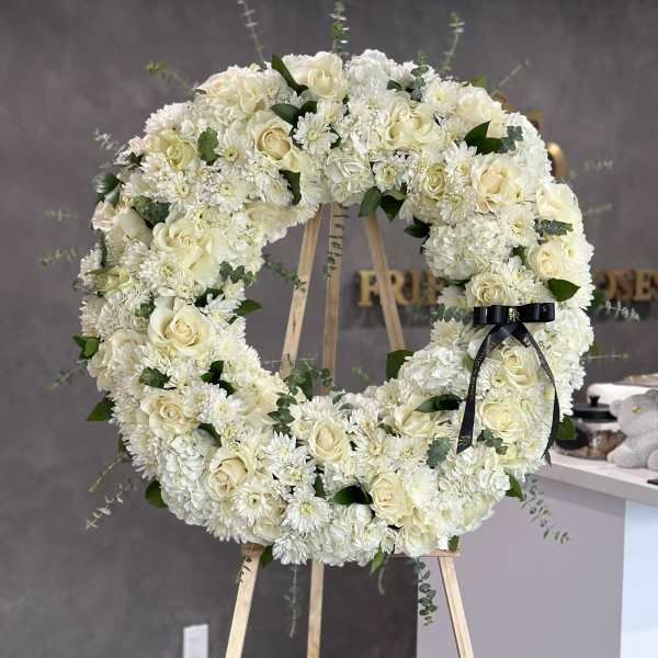 Large white floral wreath on a wooden easel with a black ribbon.