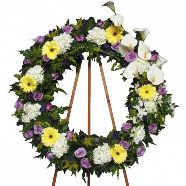 Large floral wreath with white calla lilies, yellow daisies, and purple roses on a stand