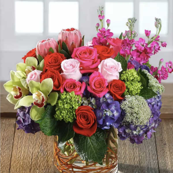 Mixed bouquet of roses, orchids, hydrangeas, and protea in a glass vase