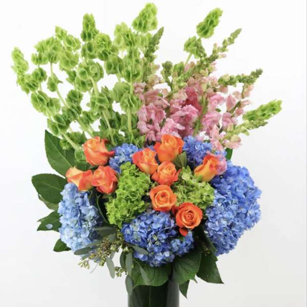 Bouquet of blue hydrangeas, orange roses, and pink snapdragons in a glass vase