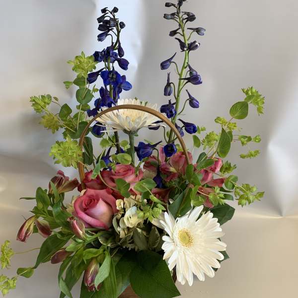 Basket arrangement with pink roses, white daisies, and blue flowers