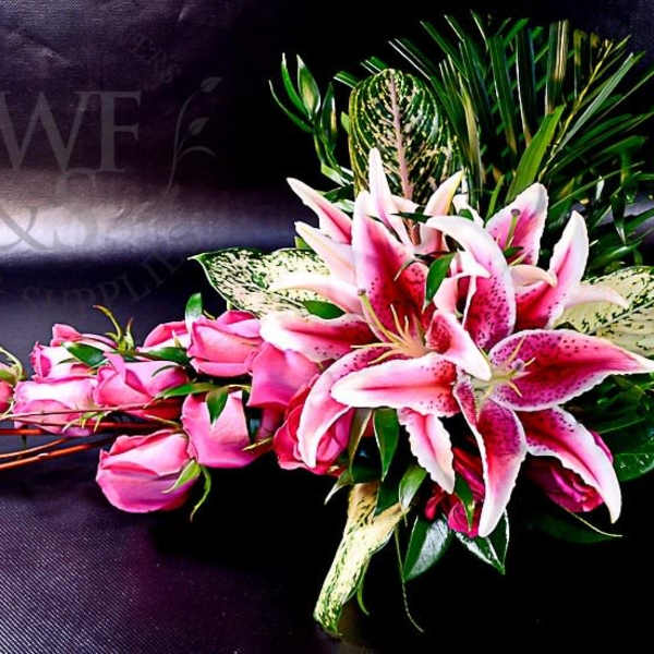 Pink roses and stargazer lilies arranged with greenery on a dark surface.