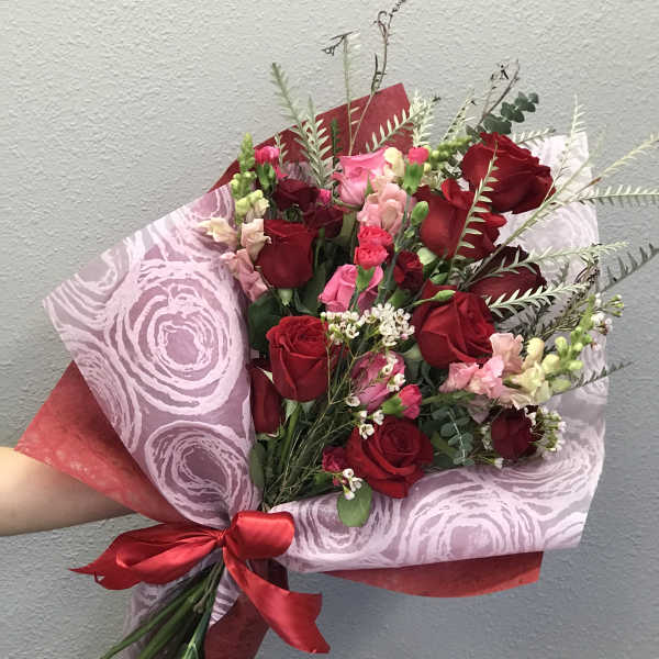 Bouquet of red and pink roses wrapped in patterned paper with a red ribbon