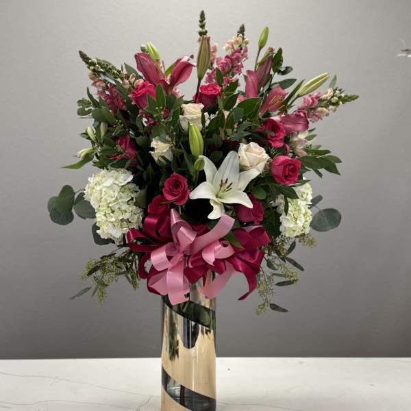 Tall bouquet of pink roses and white lilies in a gold vase with a pink ribbon