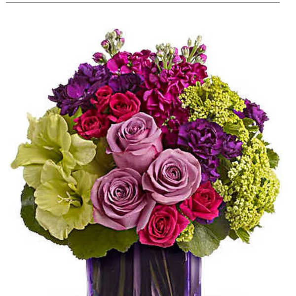 Purple and pink roses with green blooms in a purple glass vase