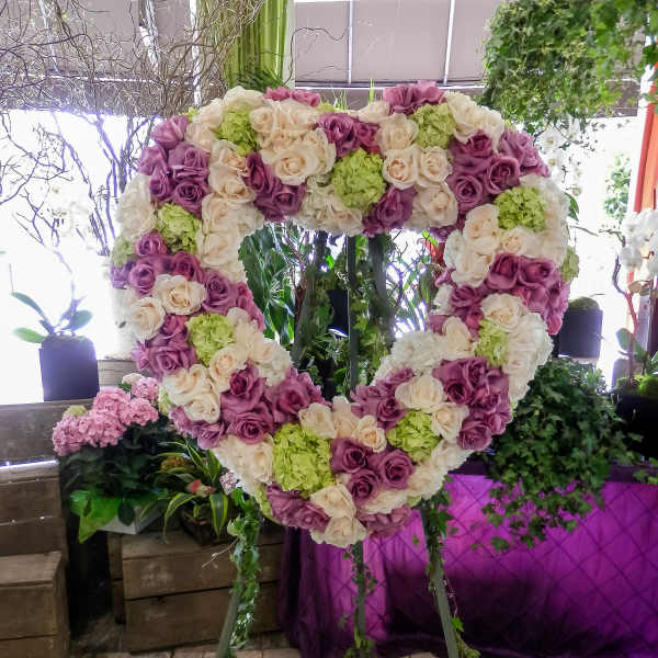 Heart-shaped floral display of pink, cream, and green roses on a stand
