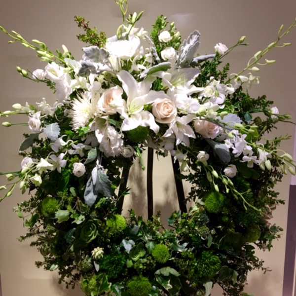 Large white floral wreath on an easel with roses and lilies