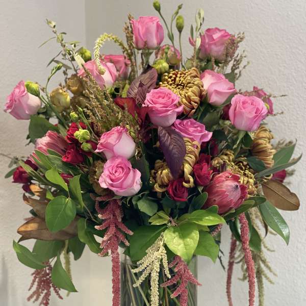 Pink roses and mixed blooms arranged in a clear glass vase