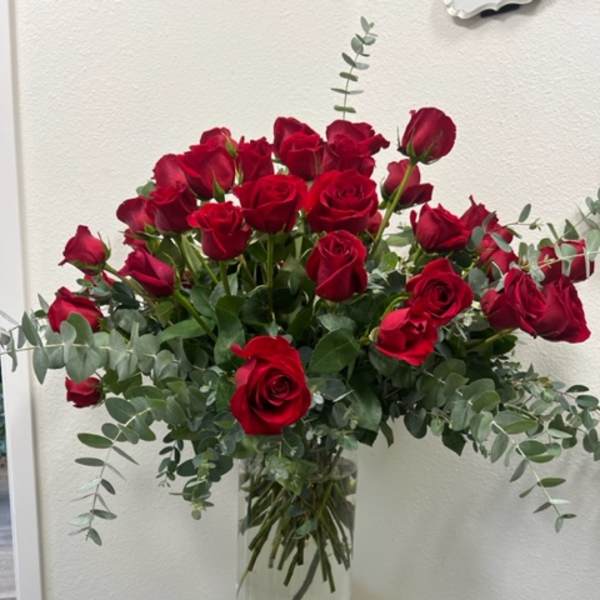 Red roses arranged in a clear glass vase with eucalyptus