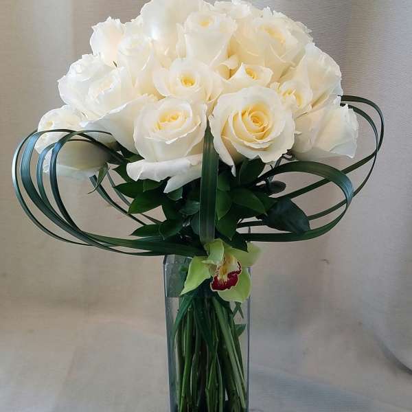 White rose bouquet in a tall glass vase with looping green leaves