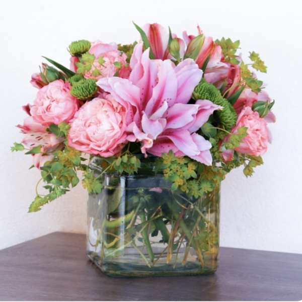 Pink lilies and roses arranged in a square glass vase