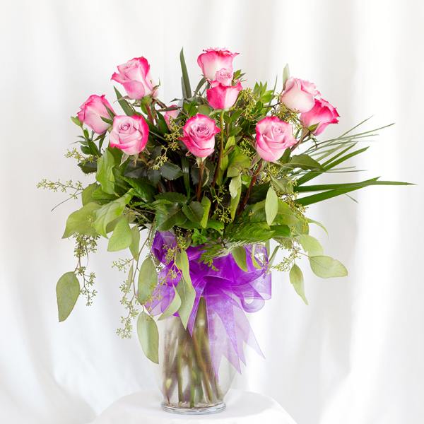Pink roses in a glass vase with a purple ribbon