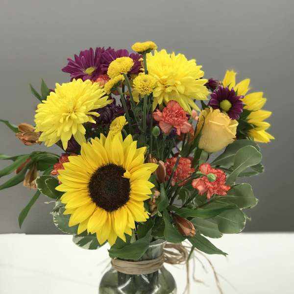 Mixed bouquet with sunflowers, purple daisies, and a yellow rose in a glass vase