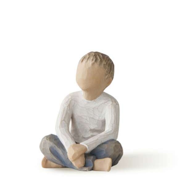 Wooden figurine of a seated child in a white shirt and blue pants