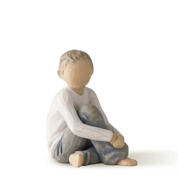 Wooden figurine of a seated child in a white shirt and blue pants