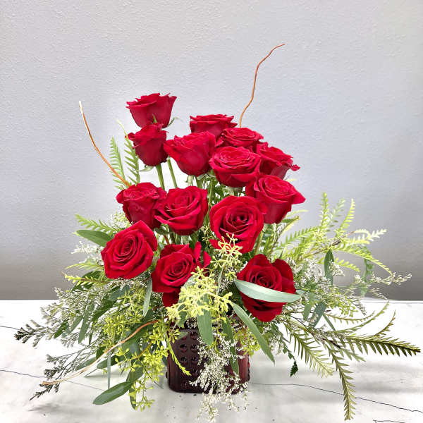 Red roses arranged in a burgundy vase with airy greenery