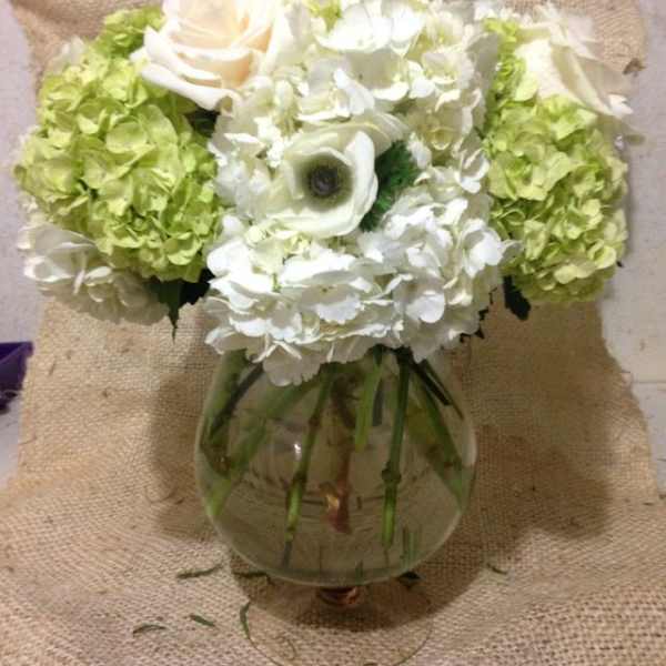 White and green floral arrangement in a round glass vase