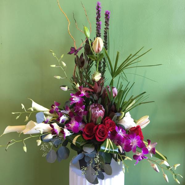 Tall floral arrangement with red roses, purple orchids, and white calla lilies in a white vase