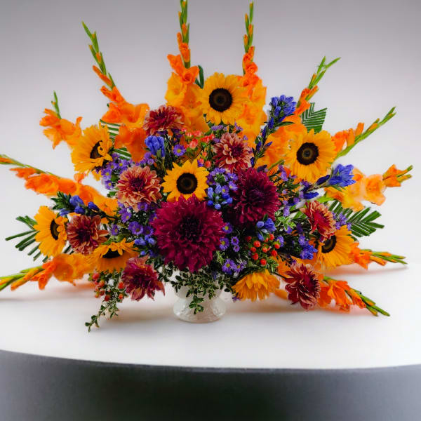Bright mixed bouquet with sunflowers, orange gladiolus, and purple blooms in a clear vase
