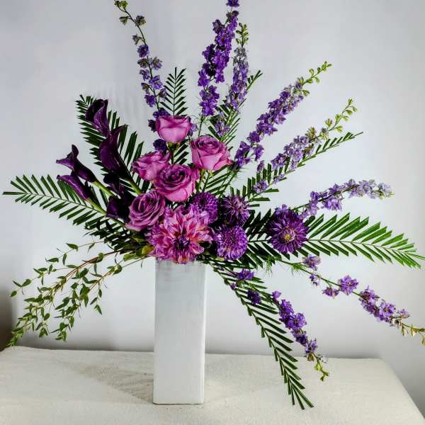 Purple roses and mixed blooms arranged in a tall white vase