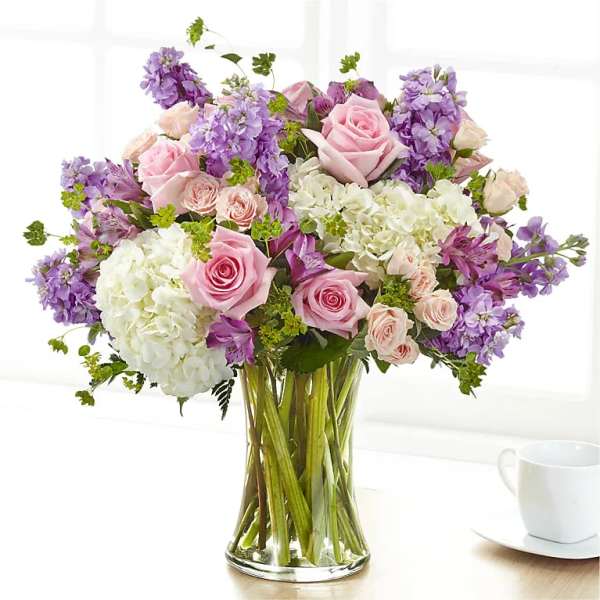 Pink roses and purple flowers arranged in a clear glass vase