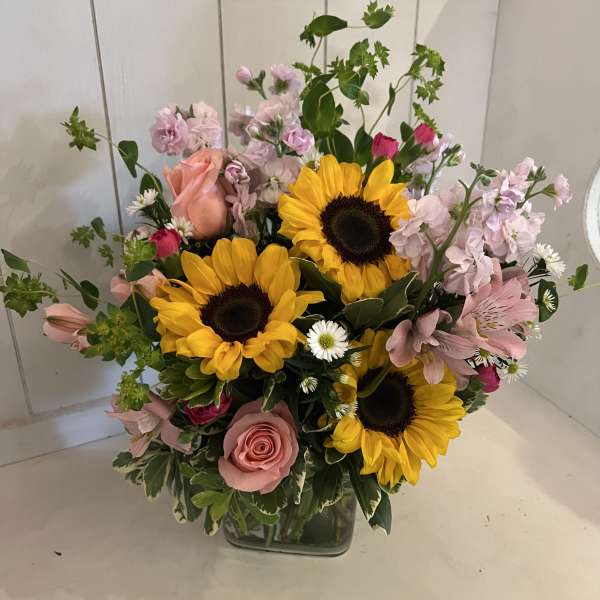 Mixed bouquet with sunflowers, pink roses, and pale pink blooms in a glass vase