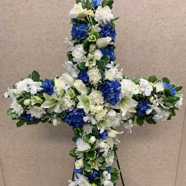 Cross-shaped floral tribute with white and blue flowers on a stand