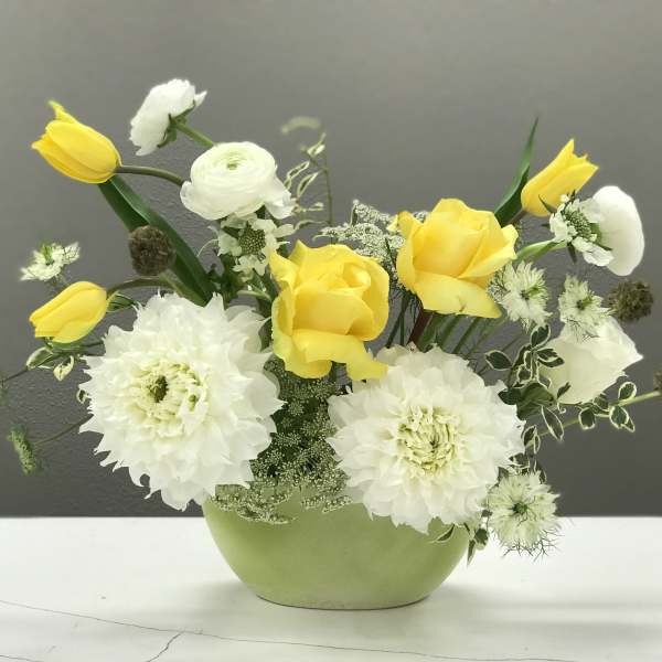 Yellow tulips and white flowers arranged in a green vase