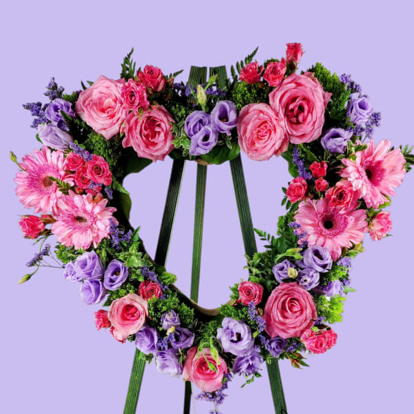 Heart-shaped floral wreath on a green easel with pink and purple flowers