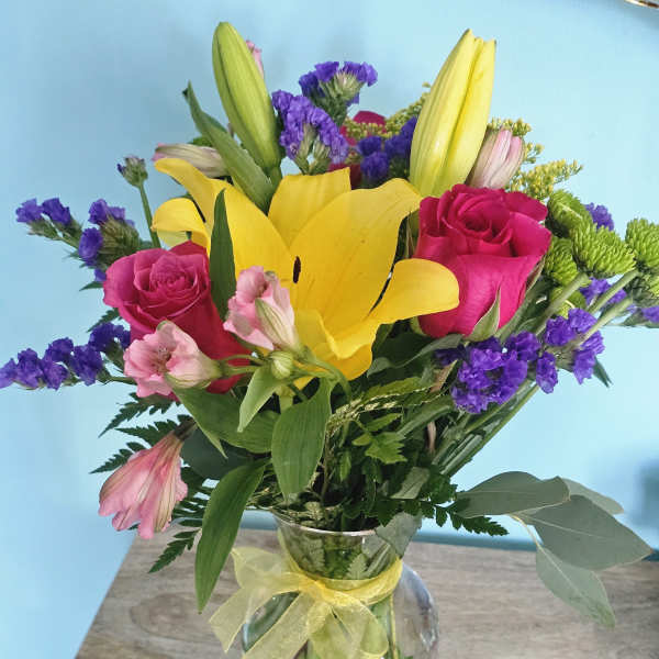 Bouquet of yellow lilies, pink roses, and purple filler flowers in a glass vase